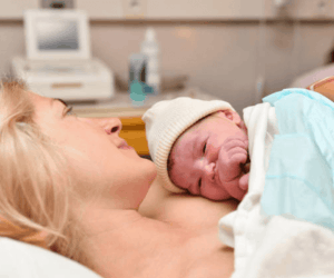 mother laying down and holding newborn baby in hospital