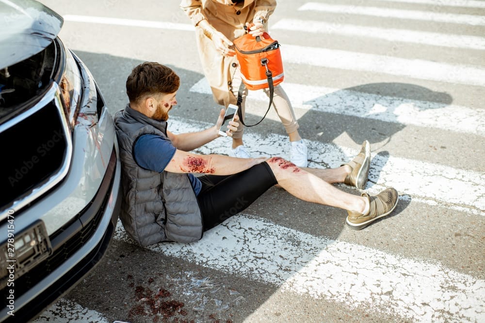 Injured man sitting near car on crosswalk.