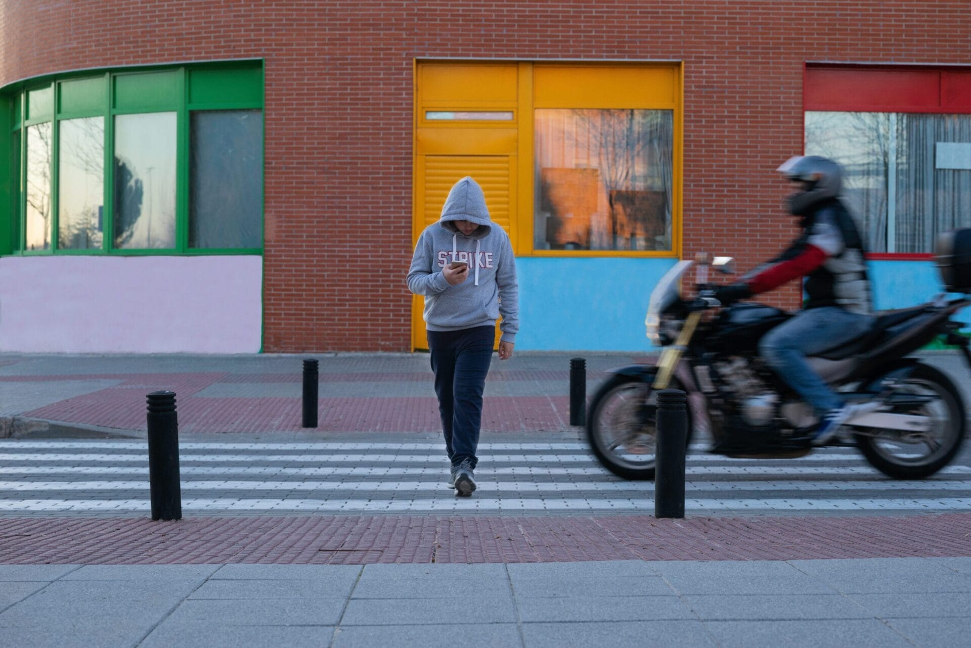 Caucasian boy about to be hit by a motorbike at a pedestrian crossing as he is distractedly looking at his mobile phone. Concept of road safety education.