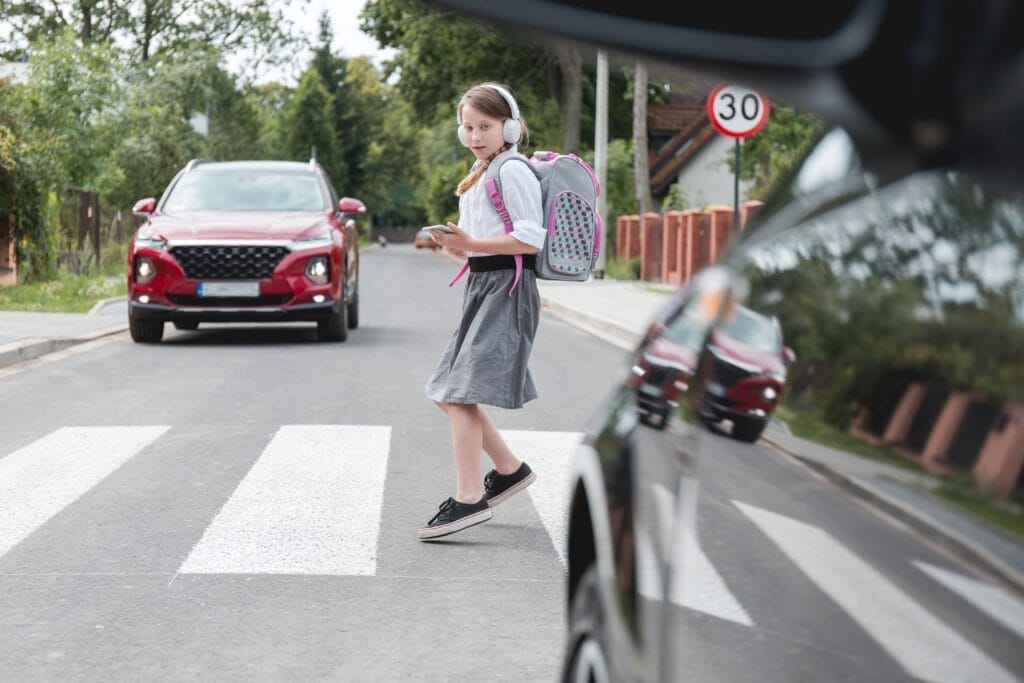Scared girl with phone and headphones runs away from the car at a pedestrian crossing
