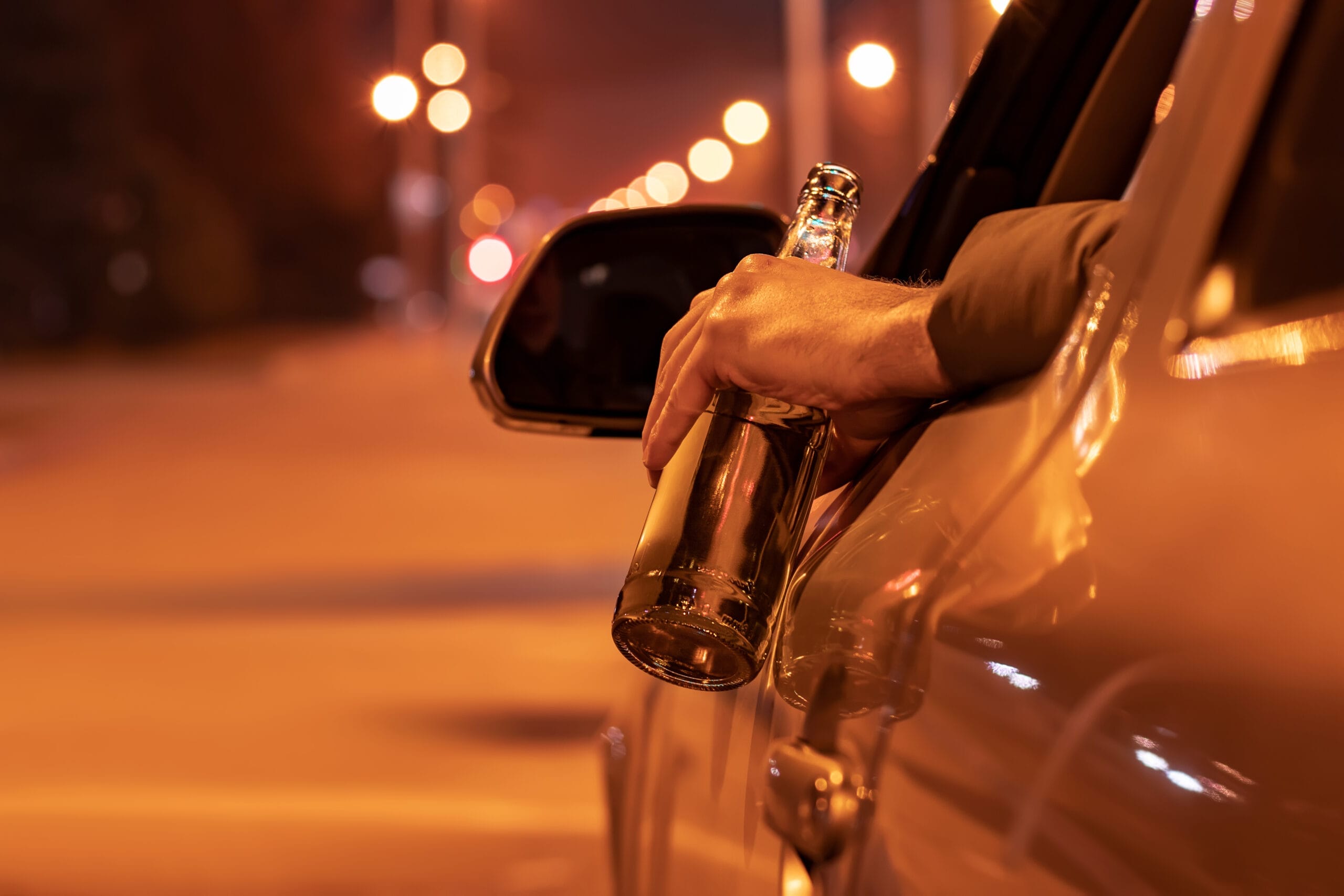 Drunk man driving a car with a bottle of beer at the night. Don't drink and drive concept.