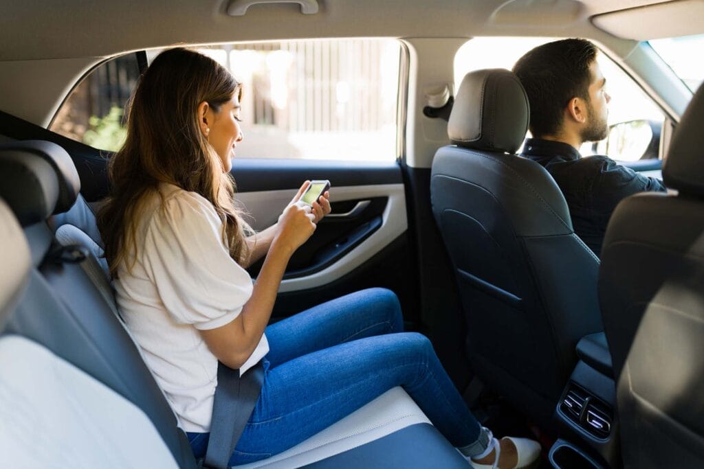 Woman using phone in car's backseat with Uber driver.